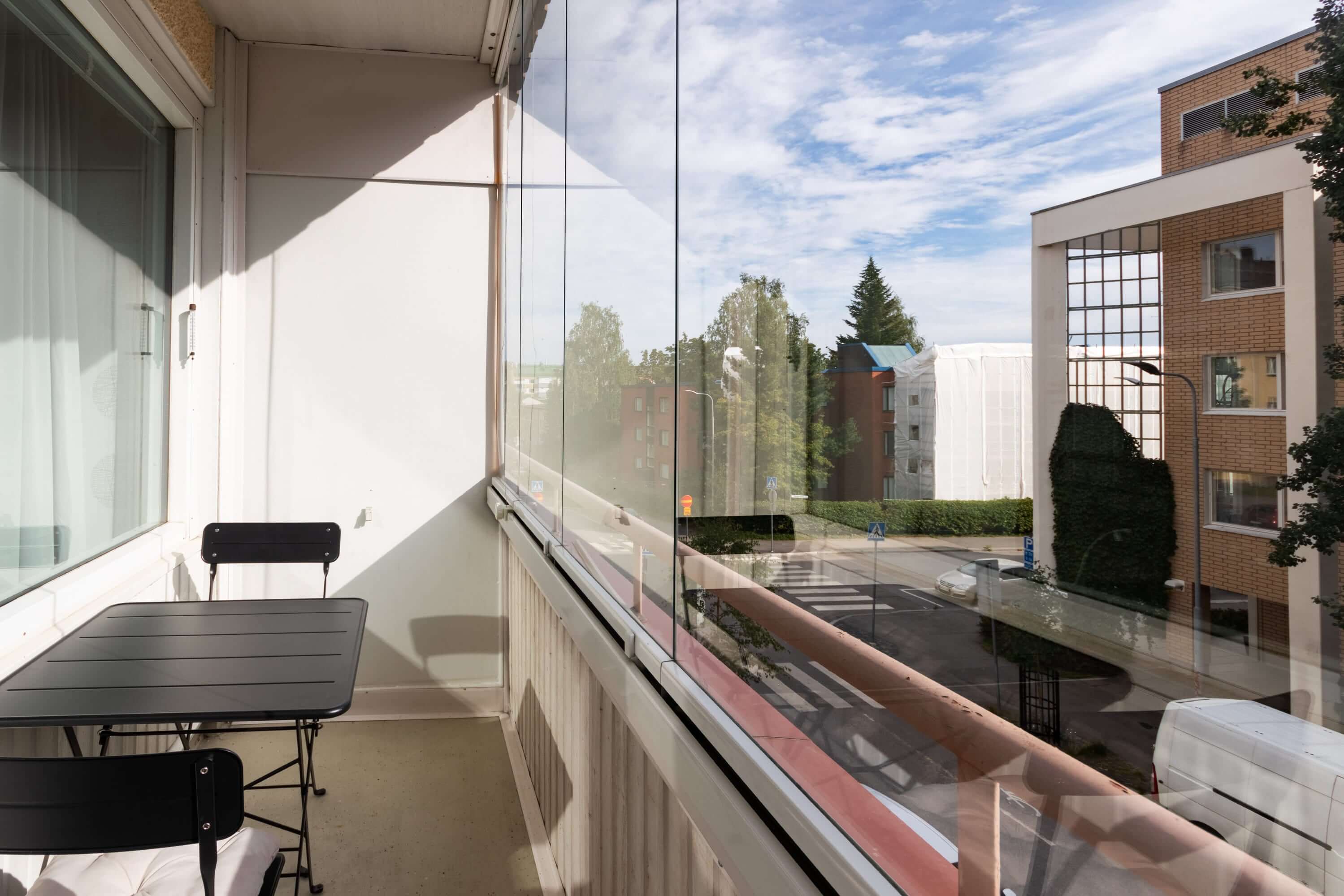 Asuntokuvaus, tilava parveke, musta pöytä ja tuolit, valoa tulviva asunnon ulkotila.