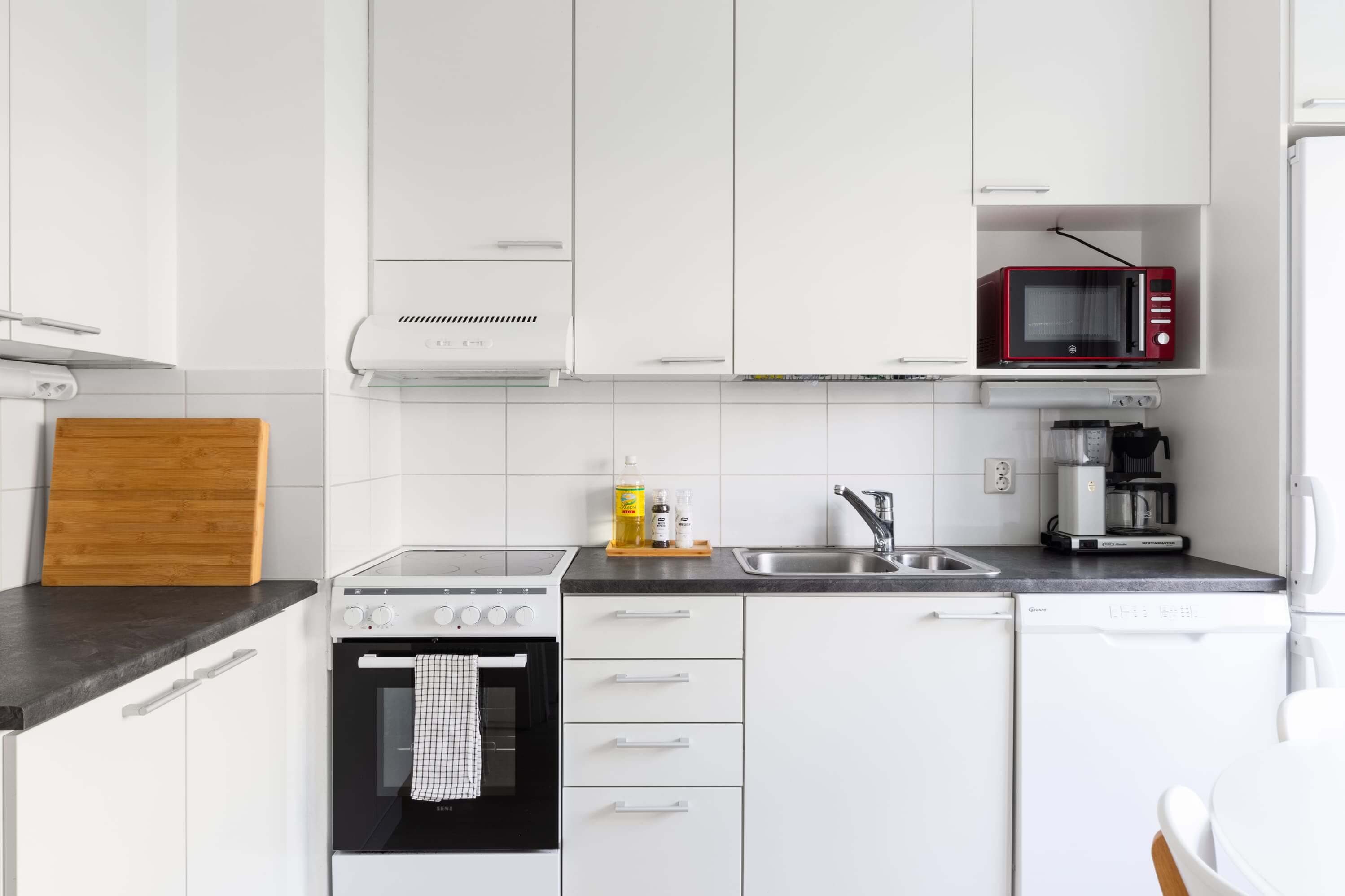 Asuntokuvaus moderni ja valoisa keittiö valkoisilla kaapeilla ja mustalla työpöydällä.