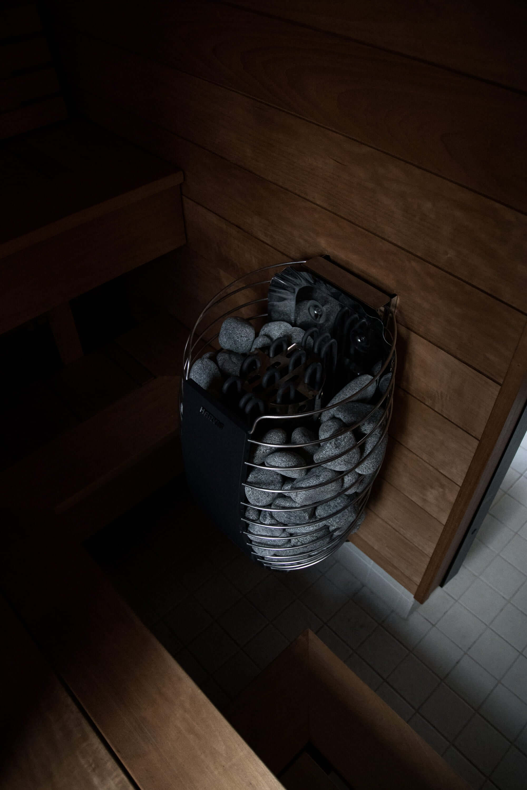 Asuntokuvaus of sauna stones and heater in a dimly lit wooden sauna interior.