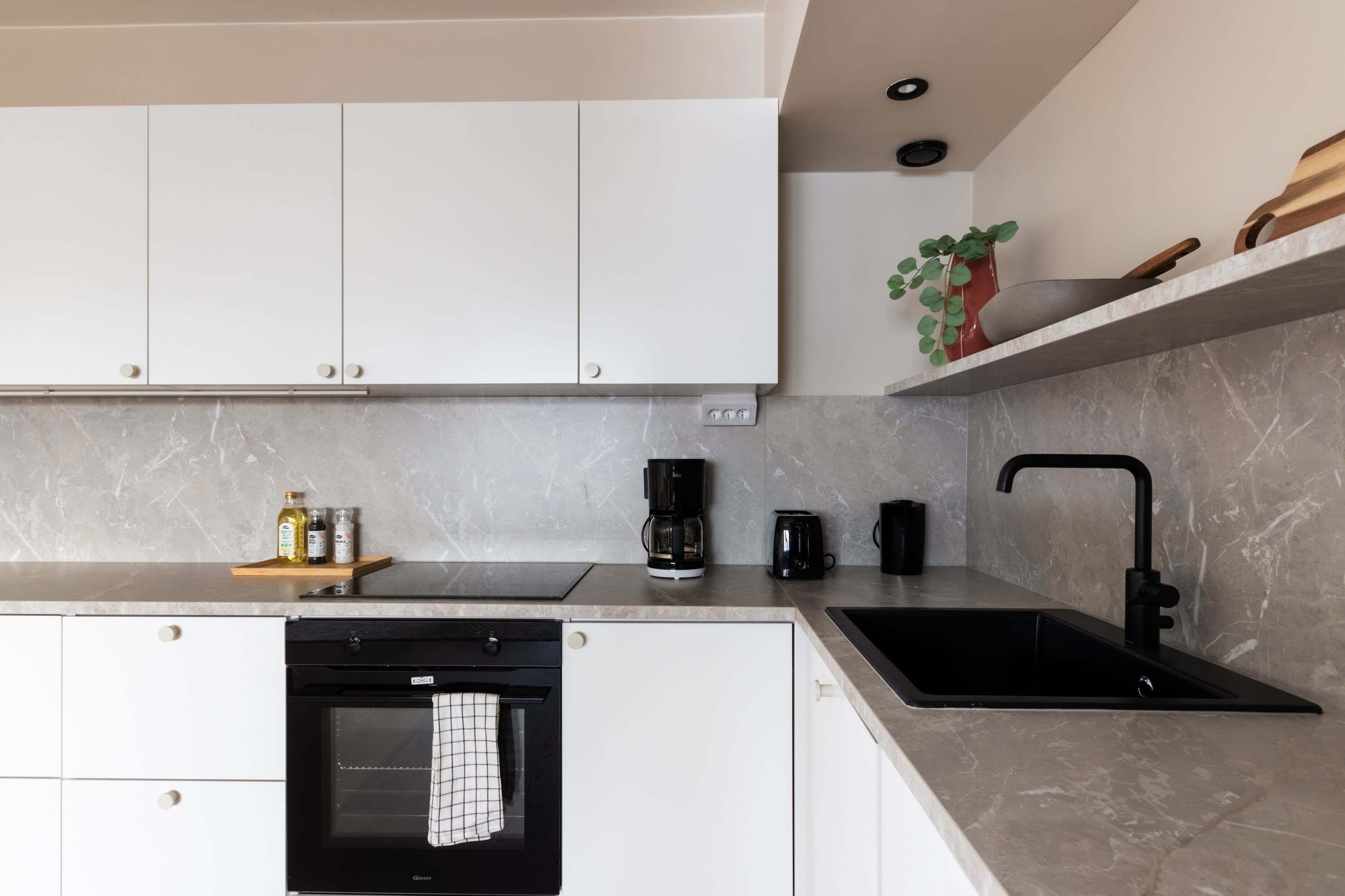 Asuntokuvaus modern kitchen with black sink, white cabinets, and coffee maker on the countertop.
