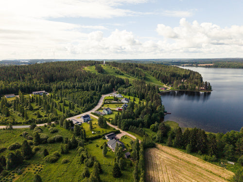 Dronekuvaus: ilmakuva omakotitaloista järven rannalla, metsää ja peltoa ympärillä